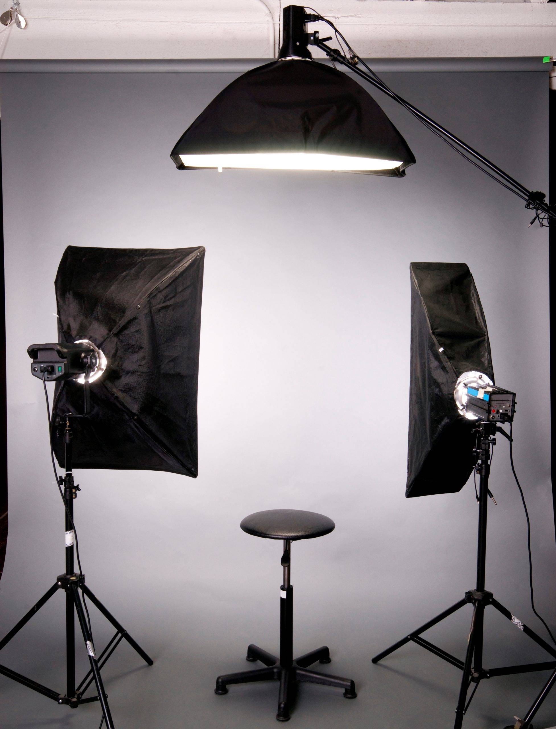 Grey photography studio background with three studio lights and black stool